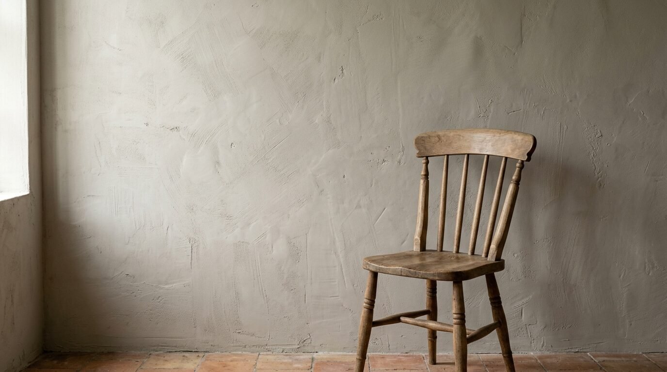 A vintage wood spindle chair placed on a terracotta tiled floor by a rustic cement plastered wall.